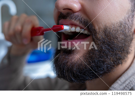 Man with beard in dental clinic holding toothbrush while cleaning teeth maintaining oral hygiene 119498575