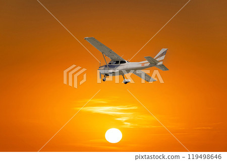 Single engine ultralight airplane flying under an orange sky at sunset 119498646