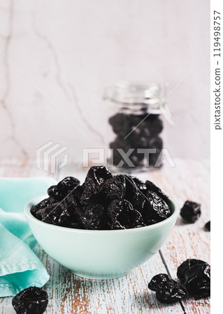 Sweet dried prunes in bowl and jar on table vertical view 119498757