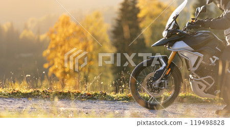 Driver posing on motorcycle during sunrise, autumn mountains 119498828