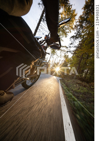 Driver riding motorcycle on empty road during sunset, autumn mountains 119498831
