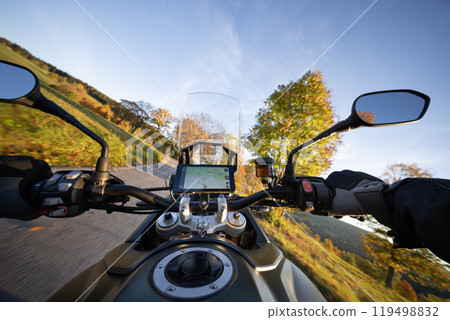 Driver riding motorcycle on empty road during sunset, handlebar view, autumn mountains 119498832