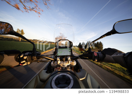 Driver riding motorcycle on empty road during sunset, handlebar view, autumn mountains 119498833