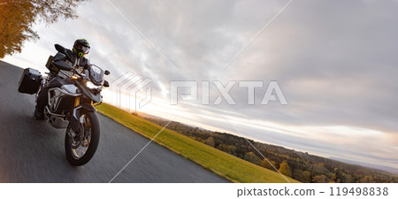 Driver riding motorcycle on empty road during sunset, autumn mountains Driver riding motorcycle on empty road during sunset, autumn mountains 119498838