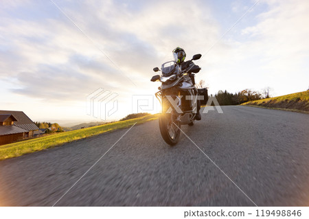 Driver riding motorcycle on empty road during sunset, autumn mountains Driver riding motorcycle on empty road during sunset, autumn mountains 119498846