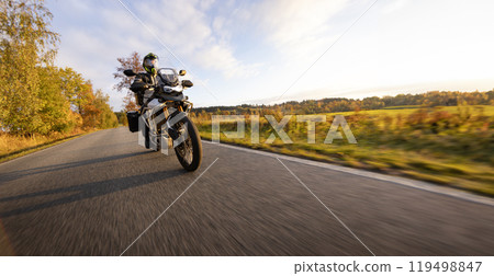 Driver riding motorcycle on empty road during sunset, autumn mountains Driver riding motorcycle on empty road during sunset, autumn mountains 119498847