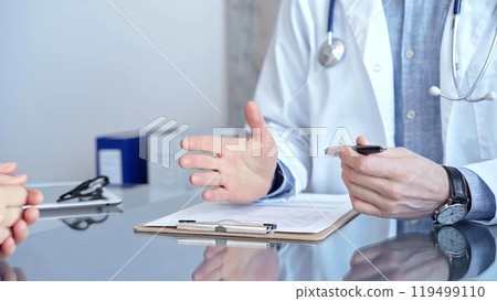 Doctor man and woman patient are discussing something and gesturing with their hands over a glass desk in medical office, close up. Medicine and Health care 119499110
