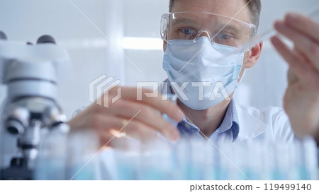 Man with safety glasses and blue mask is working with lab tubes 119499140