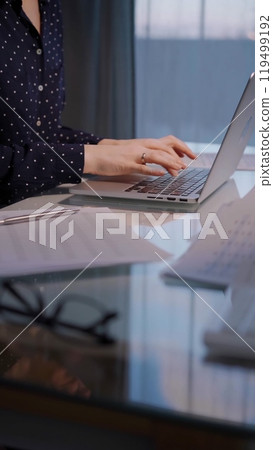 Business woman with dotted blues typing on laptop computer while sitting at the glass table in office in the evening, closeup 119499192