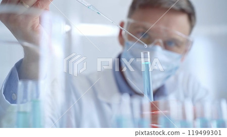 Man with safety glasses and blue mask is working with lab tubes using a pipette in a modern laboratory, close-up of researcher. Science and medicine Man with safety glasses and blue mask is working with lab tubes using a pipette in a modern laboratory, close-up of researcher. Science and medicine 119499301