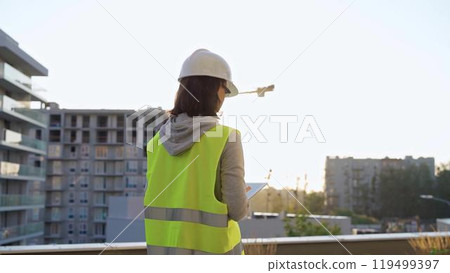 Woman construction engineer is taking notes with a tablet pc while inspecting a construction site in the morning at sunrise. Audit in architecture engineering Woman construction engineer is taking notes with a tablet pc while inspecting a construction site in the morning at sunrise. Audit in architecture engineering 119499397