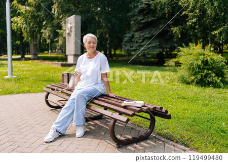Portrait of happy senior woman with short gray hair sitting on park bench, enjoying summer weather and smiling looking away. Relaxed European gray-haired older female enjoying moment of relaxation Portrait of happy senior woman with short gray hair sitting on park bench, enjoying summer weather and smiling looking away. Relaxed European gray-haired older female enjoying moment of relaxation 119499480