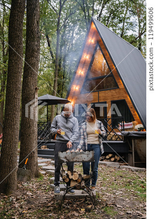 Couple grilling skewers together, enjoying barbecue in forest setting with firewood and nature Couple grilling skewers together, enjoying barbecue in forest setting with firewood and nature 119499606