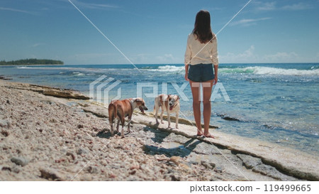 Woman and her dogs enjoy the beach, feeling the ocean breeze and listening to the waves on a sunny day. Happiness, friendship, and nature blend in this serene scene Woman and her dogs enjoy the beach, feeling the ocean breeze and listening to the waves on a sunny day. Happiness, friendship, and nature blend in this serene scene 119499665