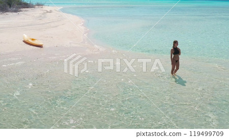 Woman is wading in the crystal clear, turquoise waters of a tropical beach, a yellow kayak resting on the white sand nearby Woman is wading in the crystal clear, turquoise waters of a tropical beach, a yellow kayak resting on the white sand nearby 119499709