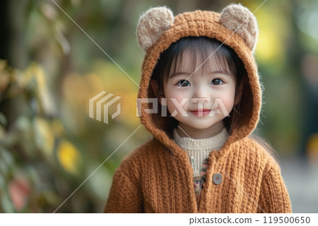 Adorable smiling asian toddler girl wearing bear hoodie outdoors 119500650