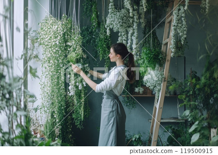 Female florist arranging white flowers hanging from ceiling in flower shop 119500915