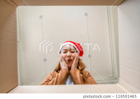 Low angle view of surprised young Asian woman wearing Christmas hat and unpacking Low angle view of surprised young Asian woman wearing Christmas hat and unpacking 119501465