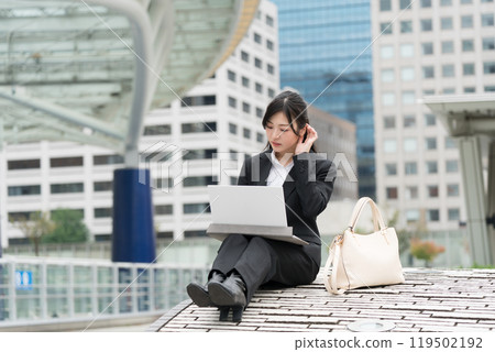 Young business woman in a suit working on a laptop outdoors Young business woman in a suit working on a laptop outdoors 119502192