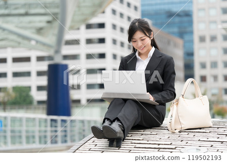 Young business woman in a suit working on a laptop outdoors Young business woman in a suit working on a laptop outdoors 119502193