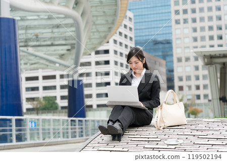 Young business woman in a suit working on a laptop outdoors Young business woman in a suit working on a laptop outdoors 119502194