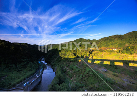 Evening view of Nunome Dam in the Yamato Plateau in eastern Nara City. Evening sky above the Nunome River with thin clouds flowing north of the dam. Evening view of Nunome Dam in the Yamato Plateau in eastern Nara City. Evening sky above the Nunome River with thin clouds flowing north of the dam. 119502258