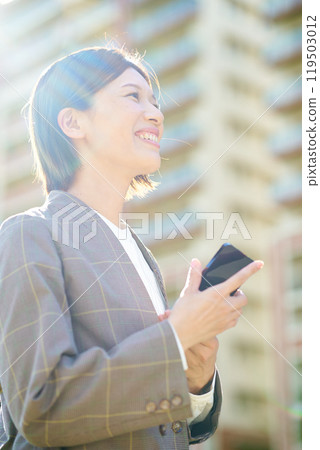 Businesswoman holding a smartphone outdoors 119503012