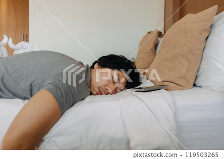 Close up face of sleepy man slept with his mobile phone left near his head. 119503265