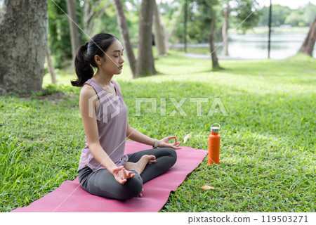 Young Woman Practicing Yoga Outdoors in a Serene Park Setting, Relaxing and Meditating on a Pink Yoga Mat Surrounded by Nature Young Woman Practicing Yoga Outdoors in a Serene Park Setting, Relaxing and Meditating on a Pink Yoga Mat Surrounded by Nature 119503271