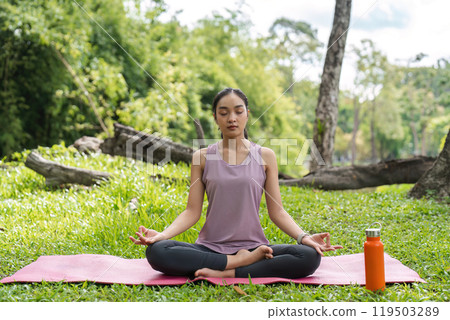 Woman Practicing Yoga Outdoors on a Sunny Day, Meditating on a Pink Mat in a Serene Green Park with Trees in the Background 119503289