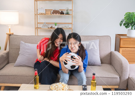 Lesbian Couple Cheering for Football Together at Home, Celebrating with Snacks and Drinks, Enjoying the Game on a Cozy Sofa in a Modern Living Room, Showing Love and Support for Their Favorite Team Lesbian Couple Cheering for Football Together at Home, Celebrating with Snacks and Drinks, Enjoying the Game on a Cozy Sofa in a Modern Living Room, Showing Love and Support for Their Favorite Team 119503293