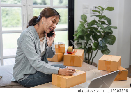 Young Woman Managing Online Sales Business, Taking Orders and Preparing Shipment in a Modern Home Office 119503298