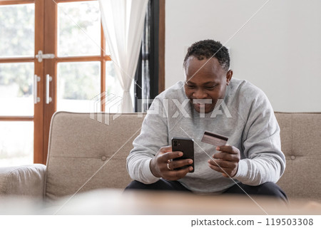 African American man using smartphone and credit card on sofa at home, Concept of mobile banking African American man using smartphone and credit card on sofa at home, Concept of mobile banking 119503308