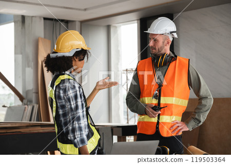 Engineering Team Discusses Construction Plans on Site with Safety Gear and Blueprints in Modern Building Interior 119503364