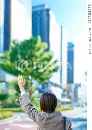 Businesswoman raising her hand on the street in a business district 119503976