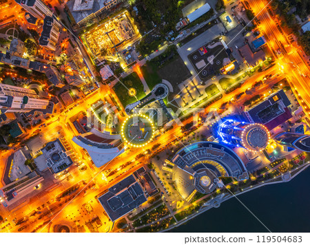 A top down, aerial view of Yekaterinburg city at night. A few vehicles are in view, surrounded by stores, restaurants, bars and warehouses. 119504683