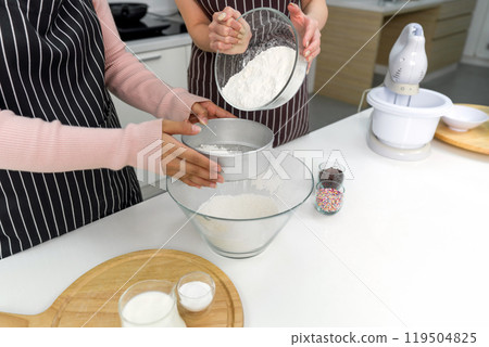 Hand sifting flour in a kitchen with baking ingredient, colorful icing and electric mixer on the side. 119504825