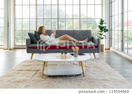 Young asian woman is relaxing on a comfortable sofa, smiling while writing down her to-do list in  living room at home. 119504869
