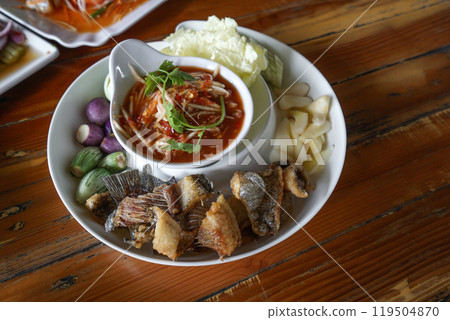 Green Mango Nam prik and Fried gourami served in compartment tray with various kinds of fresh vegetable. High angle view of dining table in Thai restaurant. Green Mango Nam prik and Fried gourami served in compartment tray with various kinds of fresh vegetable. High angle view of dining table in Thai restaurant. 119504870