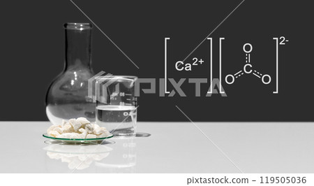 Calcium carbonate chip in chemical watch glass with molecular structure place next to beaker and Flat Bottom Flask on white laboratory table. Side view Calcium carbonate chip in chemical watch glass with molecular structure place next to beaker and Flat Bottom Flask on white laboratory table. Side view 119505036