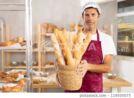 Portrait of baker holding tasty hot bread and baguettes in hands in kitchen 119505075