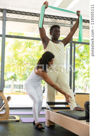Experienced Latina female instructor helping African-American man during training with resistance bands 119505111