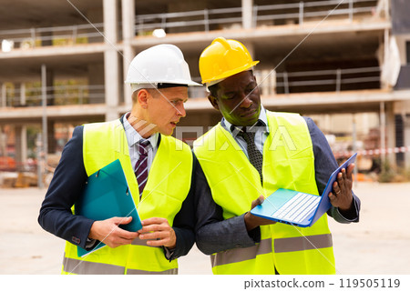 Architect and foreman must write documents and drawings on laptop with building construction Architect and foreman must write documents and drawings on laptop with building construction 119505119
