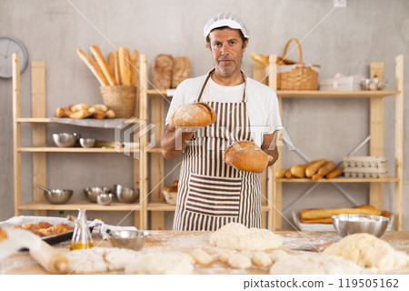 Portrait of baker holding tasty hot bread and baguettes in hands in kitchen 119505162
