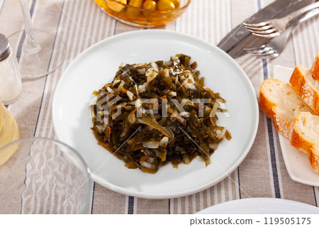 Appetizing marinated seaweed salad with onion served in plate with cutlery and bread Appetizing marinated seaweed salad with onion served in plate with cutlery and bread 119505175