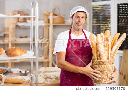 Smiling male salesman showing assortment of bakery products behind bakery counter Smiling male salesman showing assortment of bakery products behind bakery counter 119505178