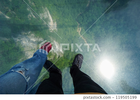 View from Zhangjiajie Grand Canyon glass bridge down to the forest below. Traveler put on shoe covers to protects the glass from getting scuffed by shoes. View from Zhangjiajie Grand Canyon glass bridge down to the forest below. Traveler put on shoe covers to protects the glass from getting scuffed by shoes. 119505199