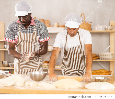 Two experienced bakers kneading and rolling dough side by side 119505282