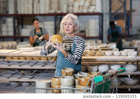 Mature craftswoman checking quality of pottery in pottery factory 119505355