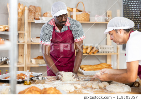 Experienced black baker kneading dough in artisan bakery 119505357
